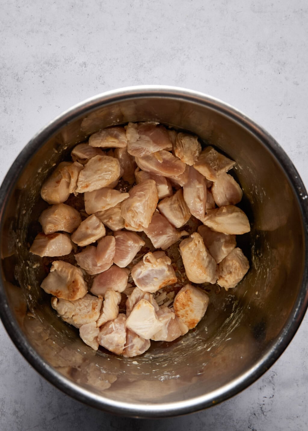 Overhead view of partially cooked chicken inside a stainless steel Instant Pot. The chicken is bite-sized.