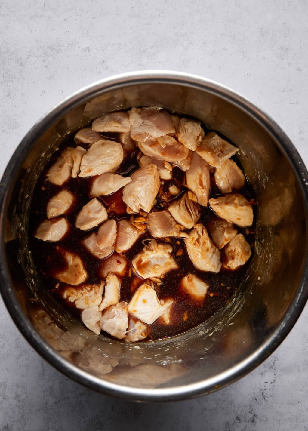Overhead view of partially cooked orange chicken inside a stainless steel Instant Pot. The chicken is bite-sized.