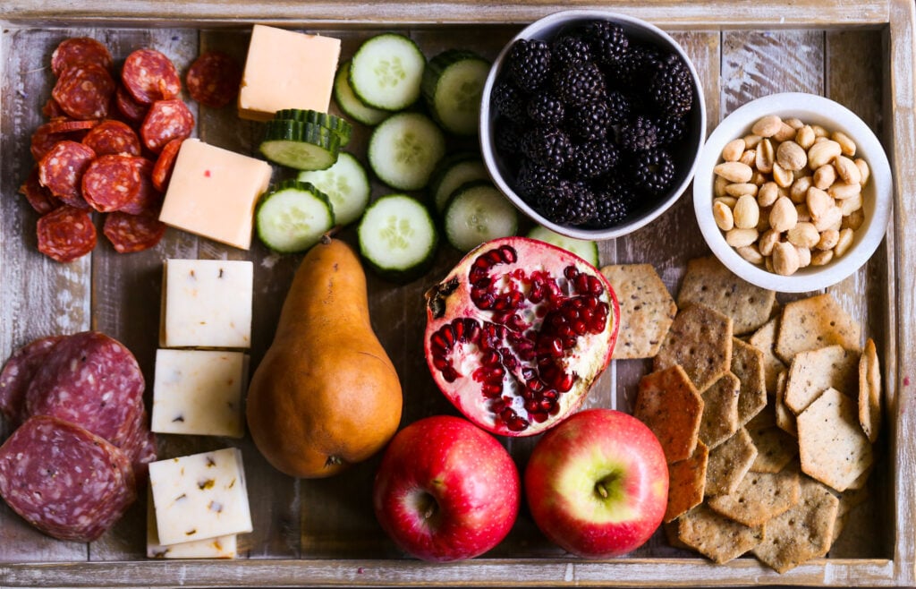 Colorful turkey charcuterie board with cheddar, gouda, salami, pepperoni, cucumbers, apples, pears, pomegranate, blackberries, crackers, and peanuts. Perfect easy Thanksgiving appetizer recipe.