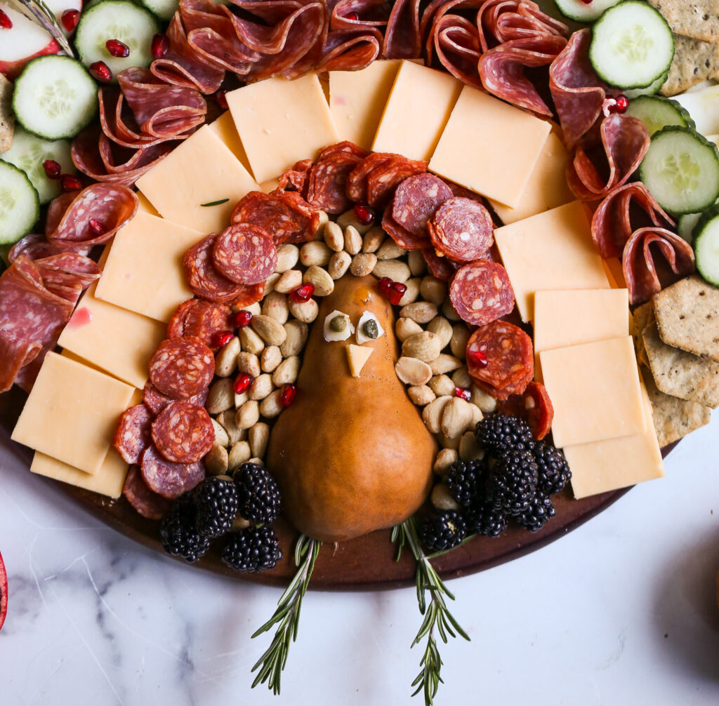 Festive turkey charcuterie board with cheddar, gouda, salami, pepperoni, pear, nuts, blackberries, and crackers. A fun Thanksgiving appetizer idea.