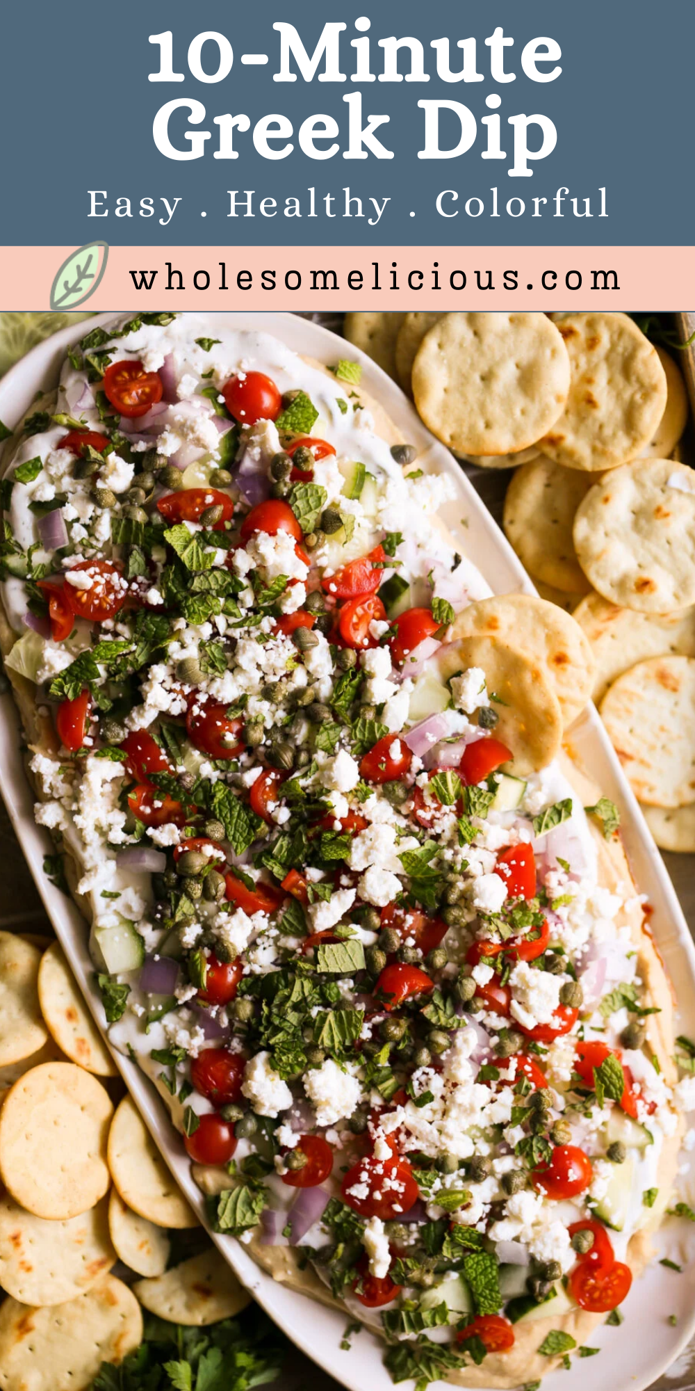 White serving dish filled with layered Greek dip featuring hummus, tzatziki, diced cucumber, cherry tomatoes, crumbled feta, capers, and fresh mint on top.