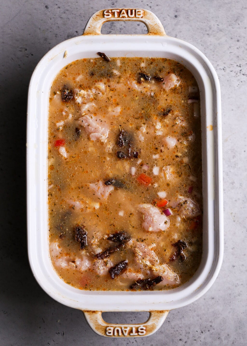 Uncooked Mediterranean chicken orzo casserole in a white baking dish, with juicy chicken, orzo pasta, sun-dried tomatoes, and herbs in broth, perfect for an easy one-pan dinner recipe.
