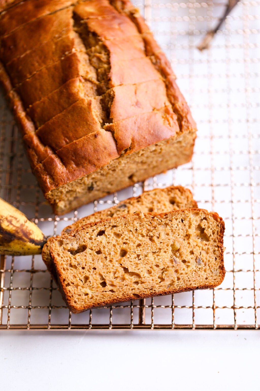 Banana bread loaf cooling on a rack, sliced piece reveals a moist, nut-studded crumb—easy banana bread recipe.