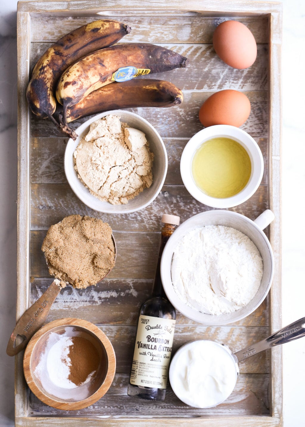 Banana bread ingredients for easy banana bread recipe: ripe bananas, eggs, flour, brown sugar, vanilla extract on rustic tray
