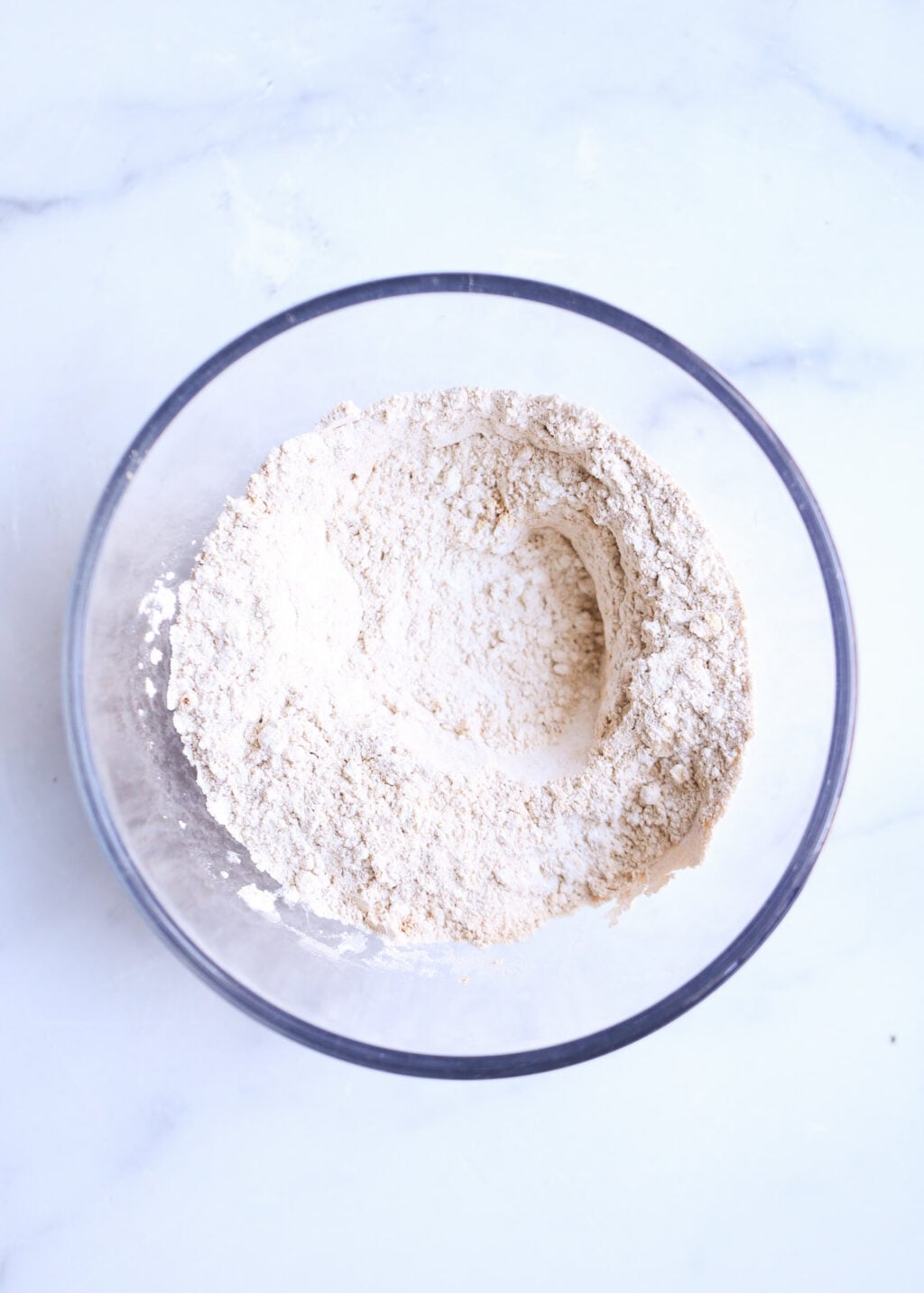 Top-down bowl of dry ingredients for high-protein peanut butter banana bread batter (flour, PBfit, cinnamon, baking soda).