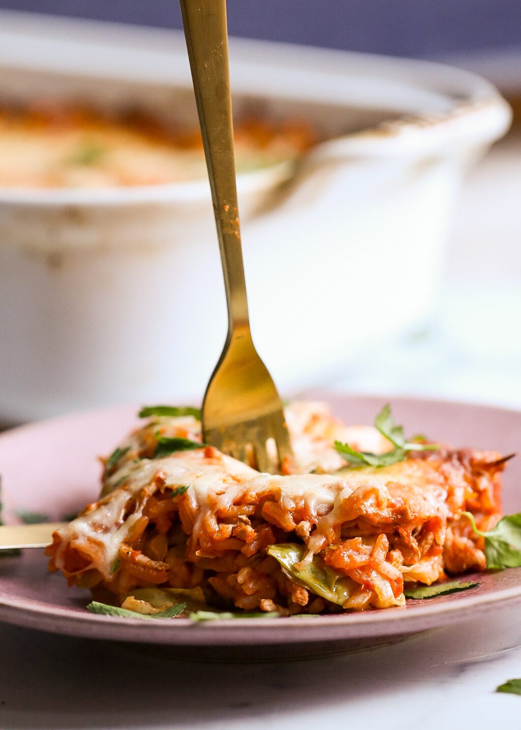 Easy unstuffed cabbage casserole with ground beef, rice, cabbage and melted cheese on a pink plate.