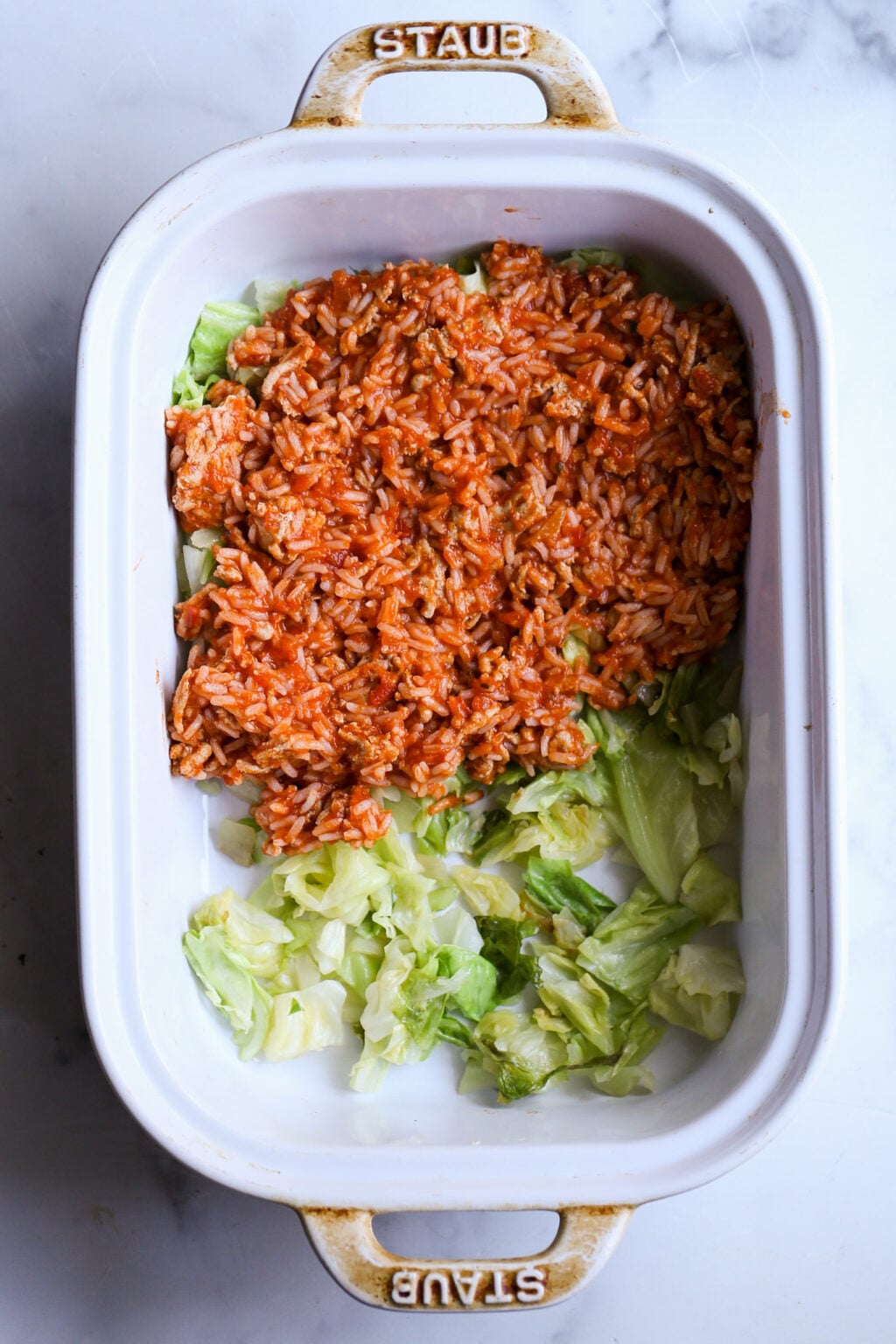 Easy unstuffed cabbage casserole with tomato rice topping over shredded cabbage in a white Staub baking dish
