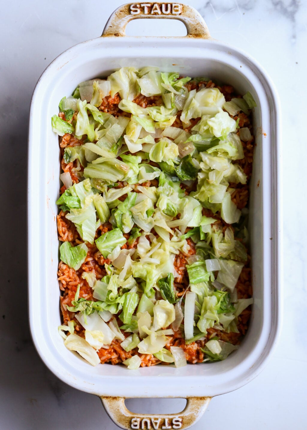 Easy unstuffed cabbage casserole with ground beef and rice, layered with chopped cabbage in a Staub dish for dinner