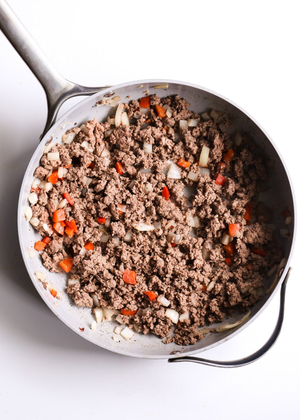 Skillet of browned ground beef with diced onions and red bell peppers, set for a healthy cheeseburger casserole dinner.
