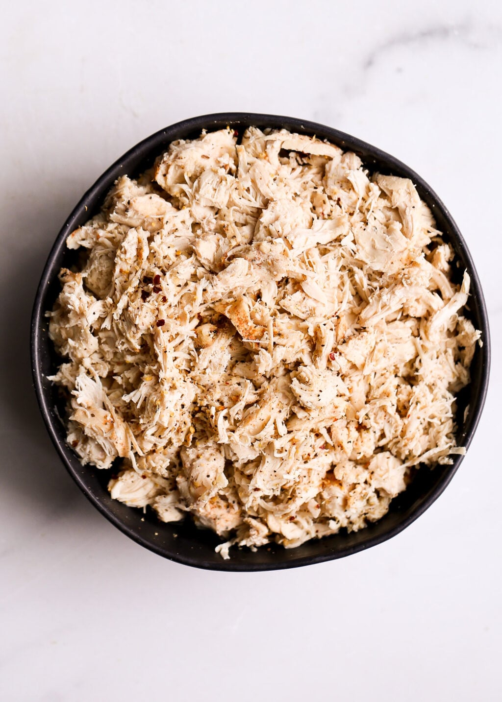 Easy slow cooker shredded chicken in a black bowl, tender seasoned chicken perfect for dinner recipes.