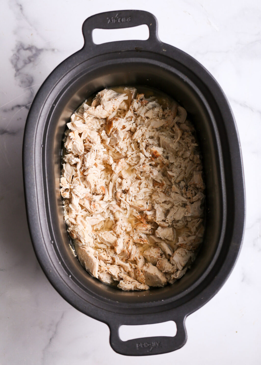Slow cooker shredded chicken in a black pot, easy dinner idea for tacos, bowls, or sandwiches