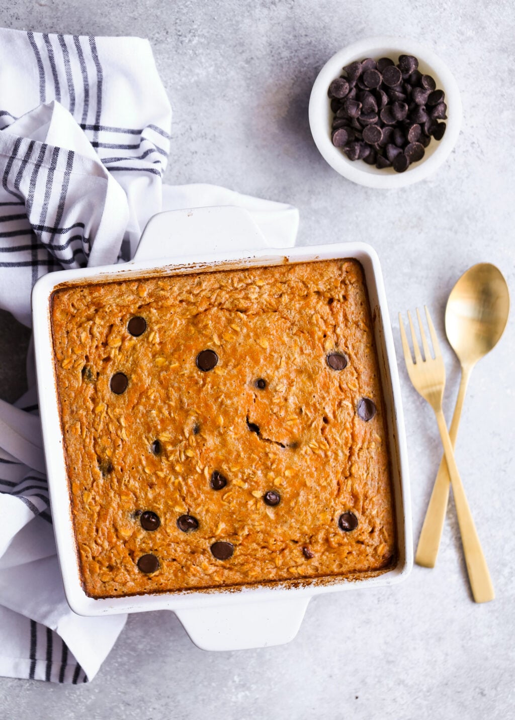 Sweet potato chocolate chip breakfast casserole in a white baking dish, chips visible on top, on a gray surface.