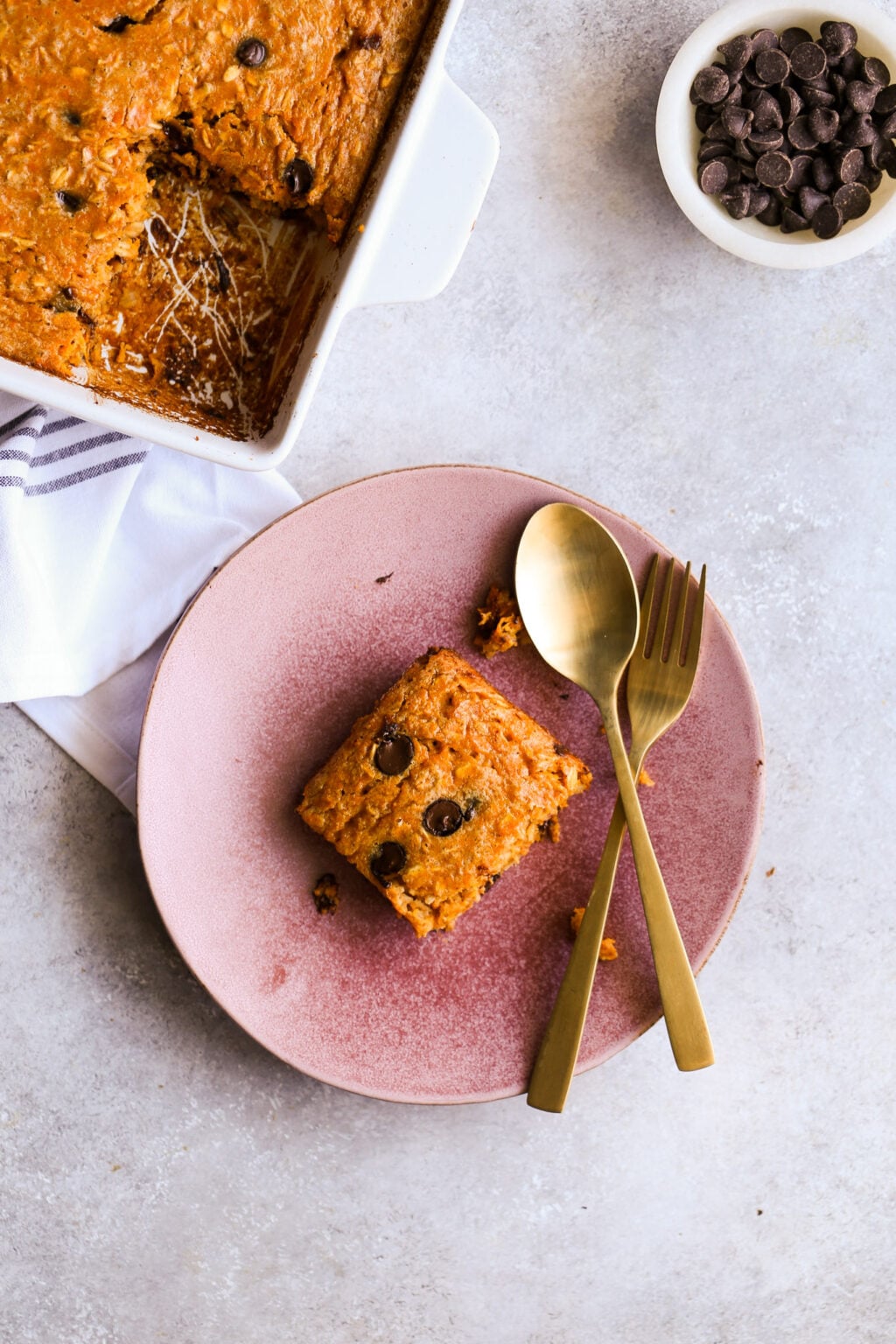 High-protein sweet potato chocolate chip breakfast casserole baked in a white dish; slice on pink plate with gold utensils.