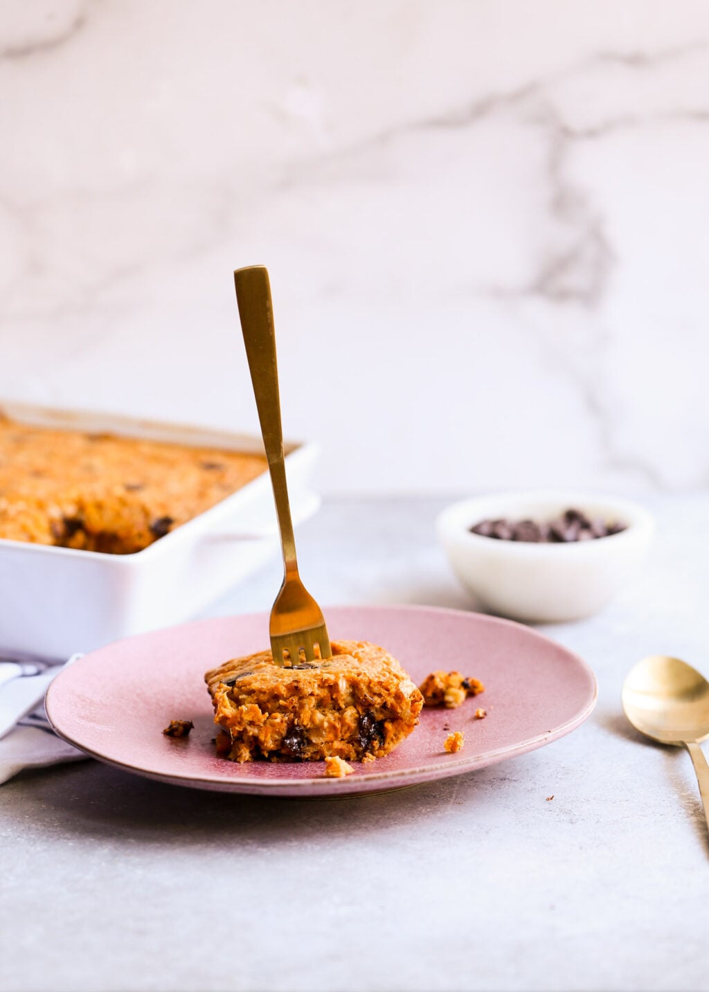 High-protein sweet potato chocolate chip breakfast casserole slice on pink plate; golden-brown bake in background.