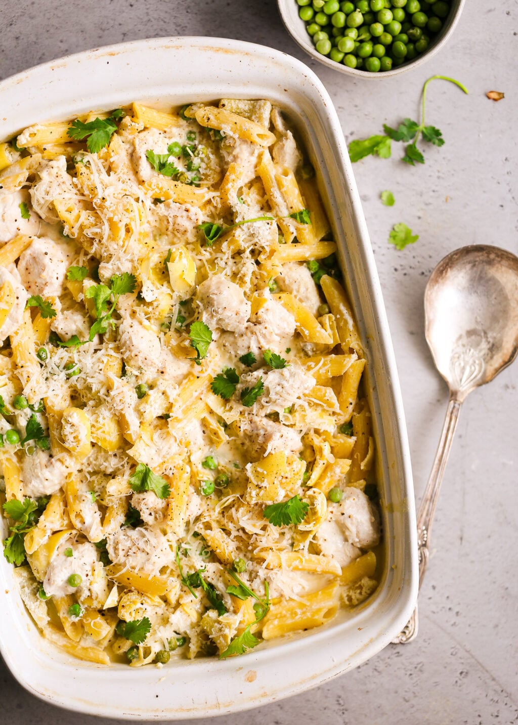 Creamy no-boil chicken pasta casserole with artichokes and peas, dump-and-bake style, topped with cheese and fresh parsley.
