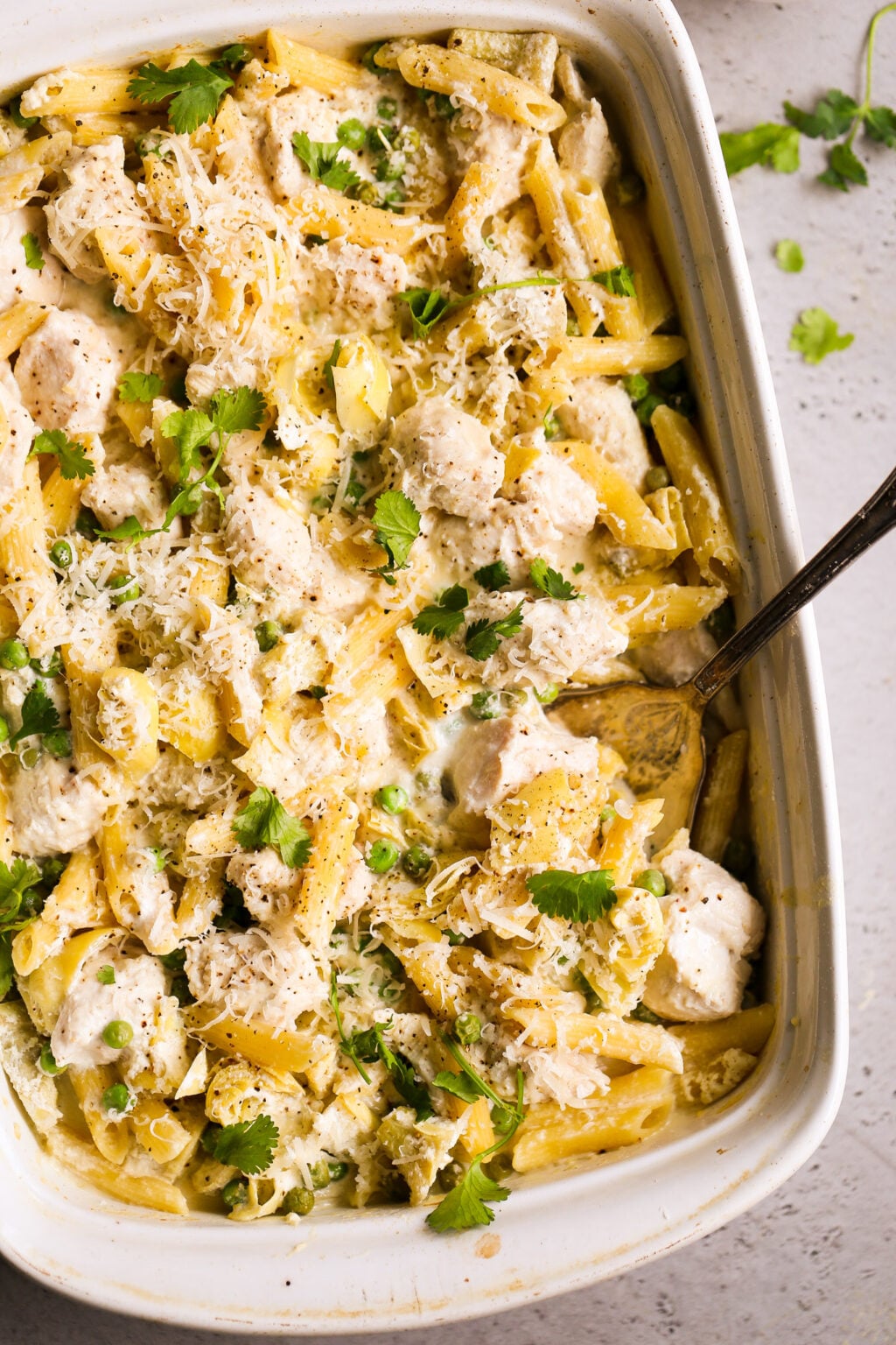Creamy no-boil chicken pasta casserole with artichokes and peas, topped with parmesan and fresh herbs.