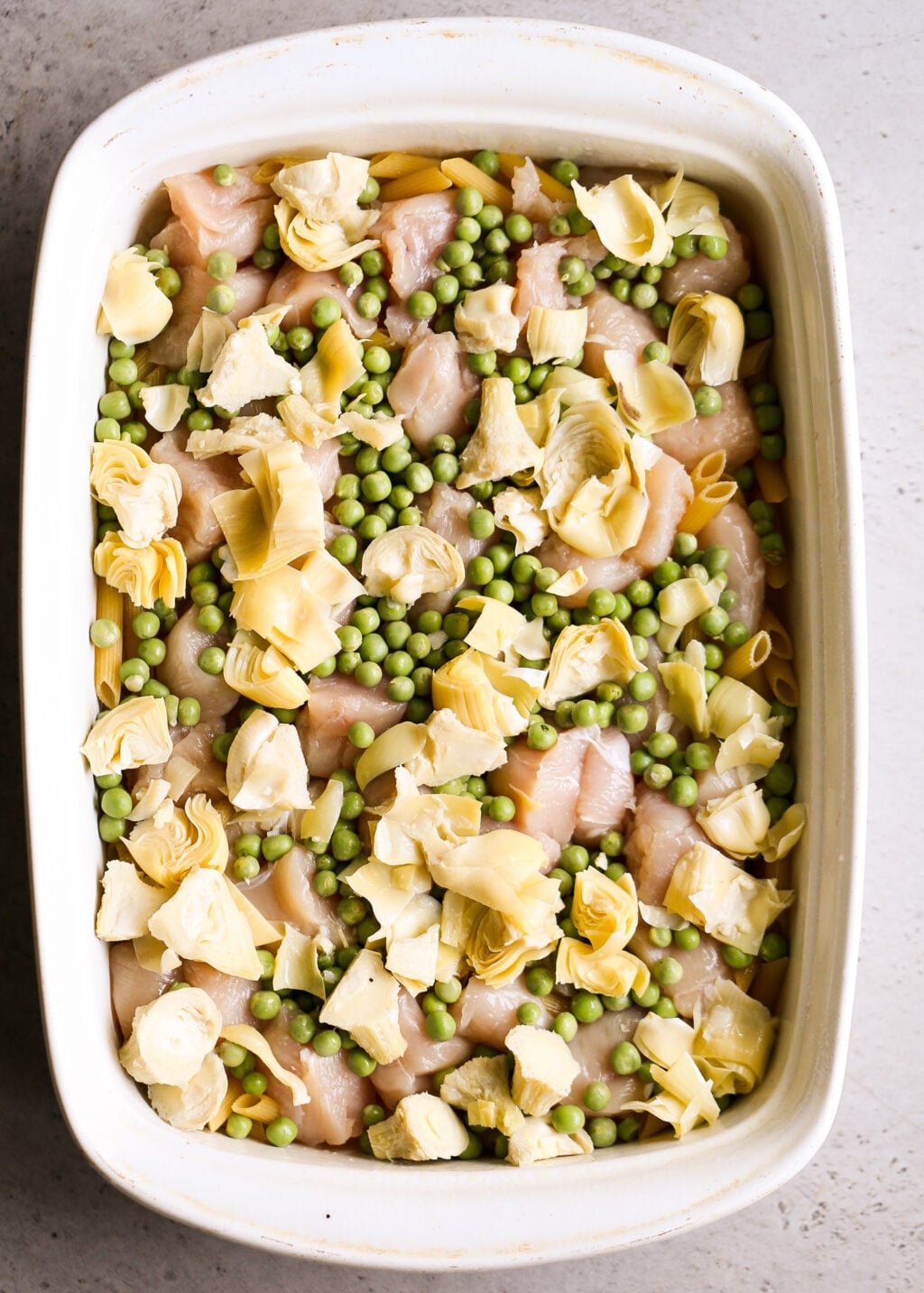 No-boil chicken pasta casserole with artichokes and peas: raw chicken, peas, artichoke hearts, and pasta in a baking dish