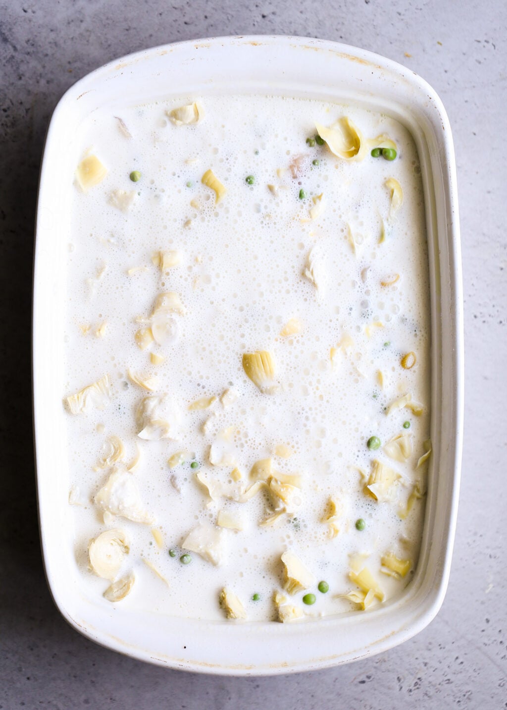 Creamy no-boil chicken pasta casserole with artichokes and peas in a white sauce, ready to bake.