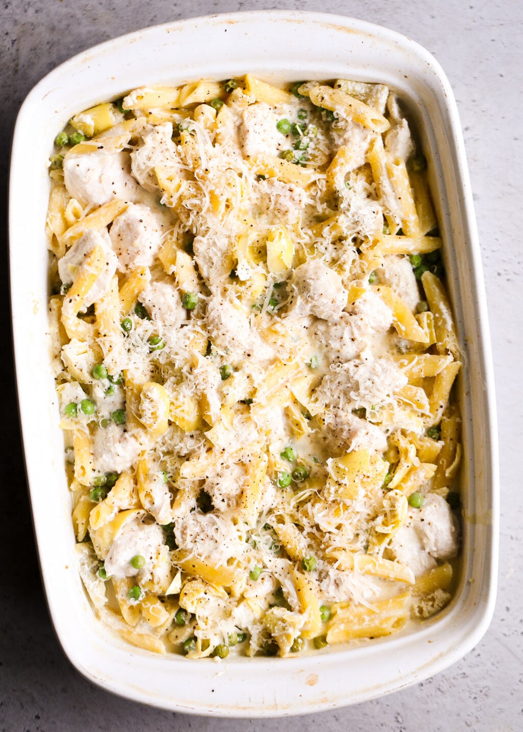 Creamy no-boil chicken pasta casserole with artichokes and peas, topped with parmesan in a white baking dish.