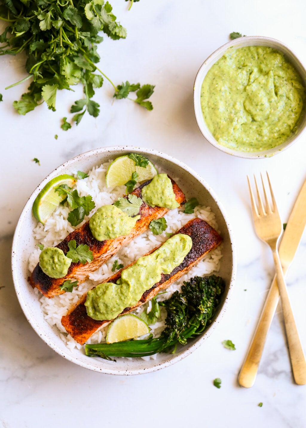 Sheet-pan blackened salmon with cilantro avocado pesto over white rice, lime wedges, and fresh cilantro.