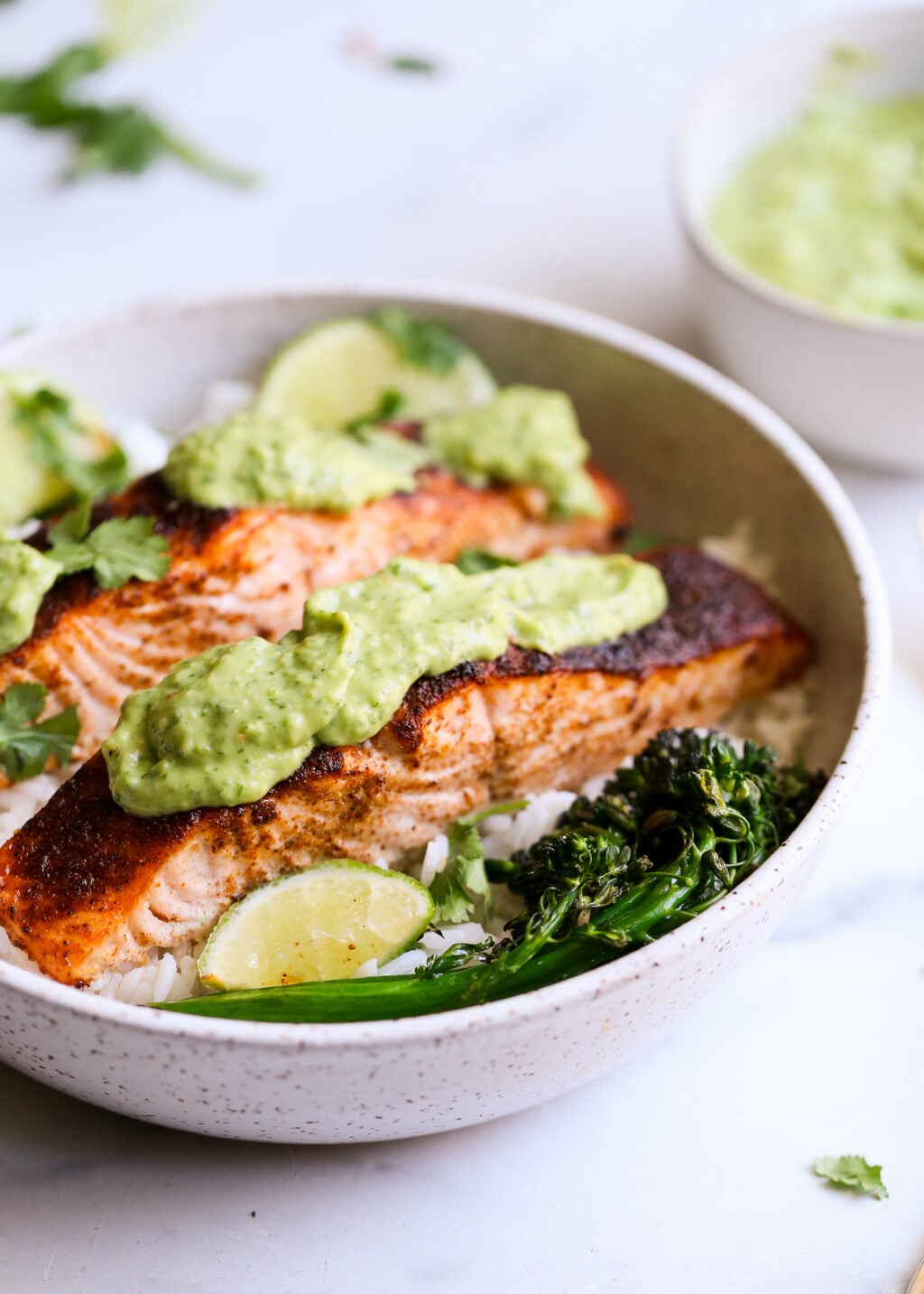 Sheet-pan blackened salmon with cilantro-avocado pesto over rice, lime wedges, and greens.