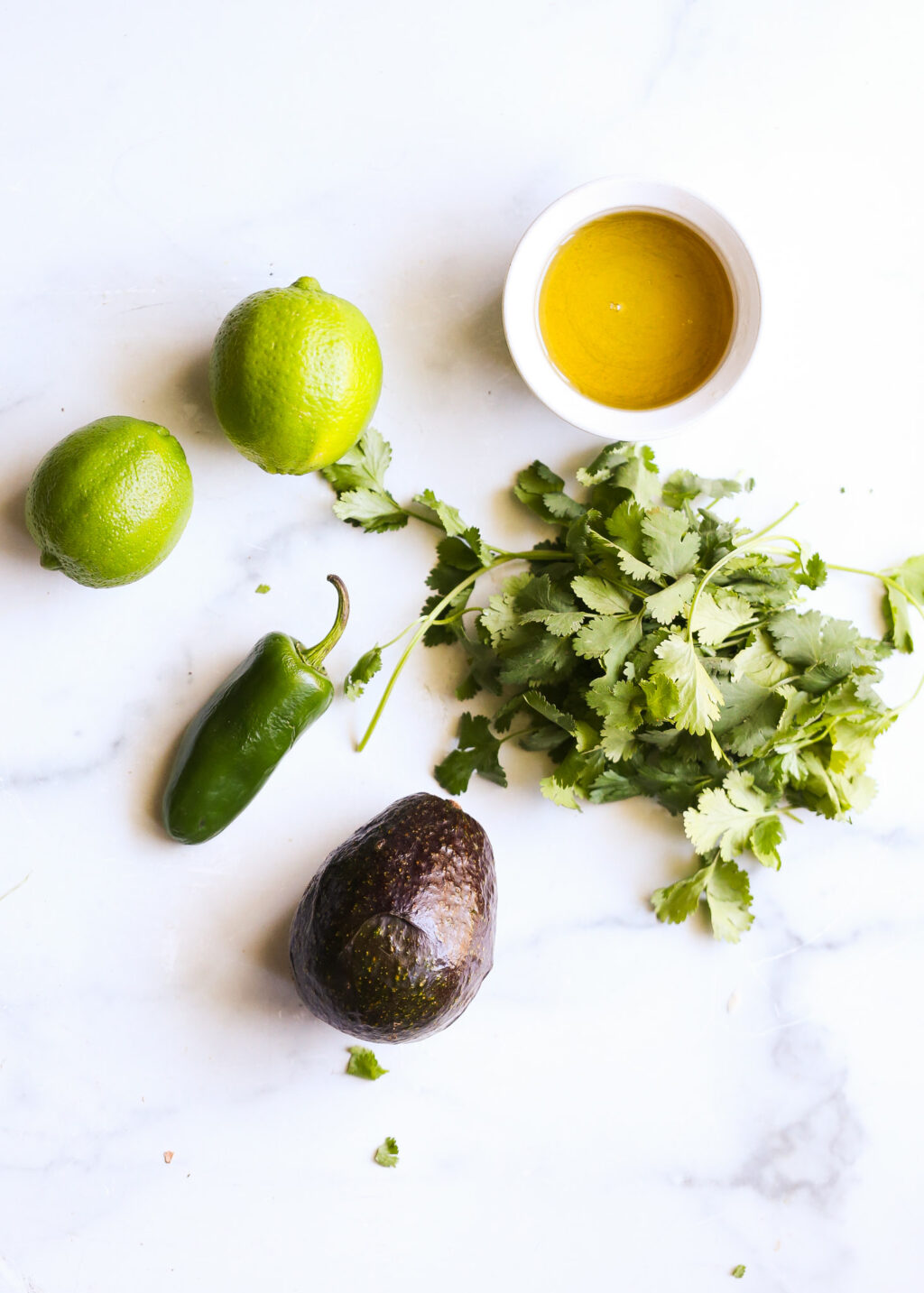 Fresh limes, avocado, jalapeño, and cilantro with a bowl of cilantro avocado pesto for sheet-pan salmon recipe.
