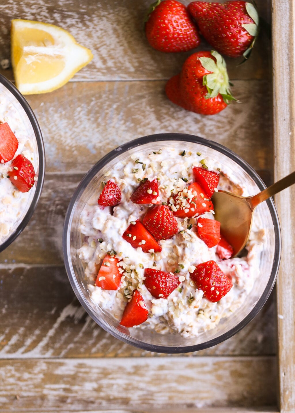 Strawberry-lemon overnight oats in glass bowls, topped with fresh strawberries and sesame seeds on a rustic wooden tray.