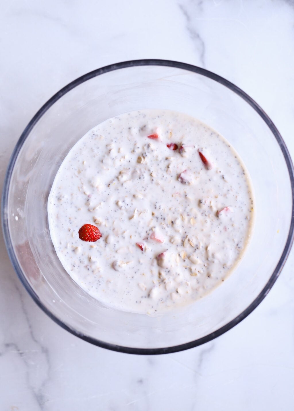 Strawberry-lemon overnight oats for breakfast in a glass bowl on white marble; creamy, no-cook oats with berries.