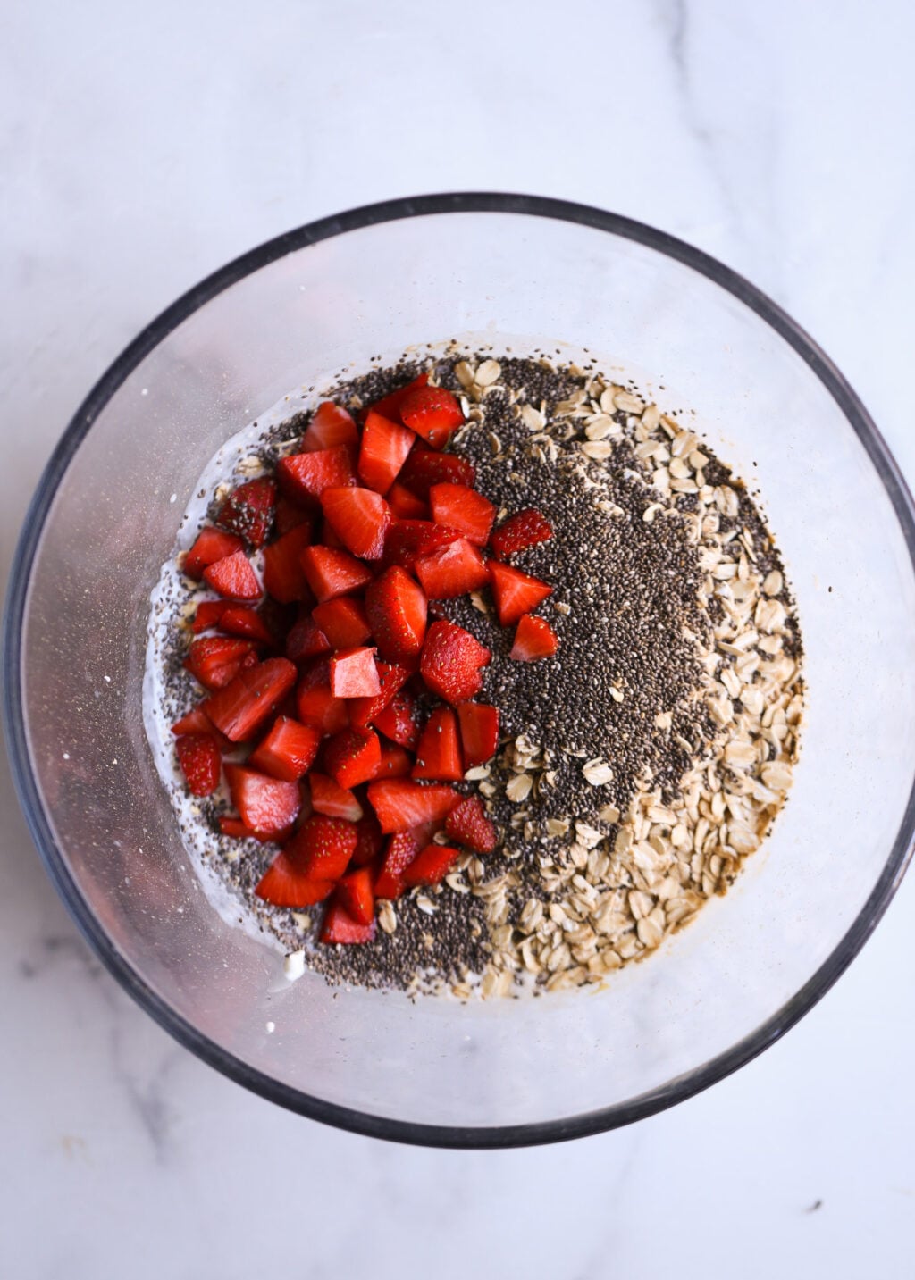 Glass bowl of strawberry overnight oats topped with chia seeds, rolled oats, and almond slices, ready for breakfast.