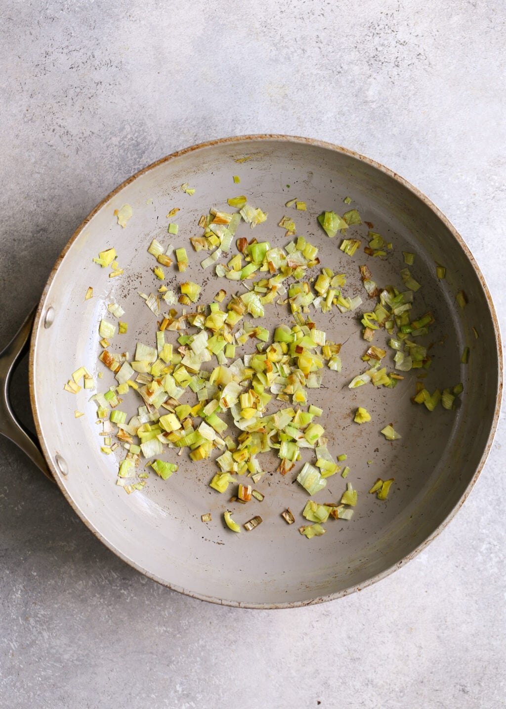 Sautéed leeks in a skillet—small pale-green and white pieces lightly browned, part of a high-protein egg muffin recipe.