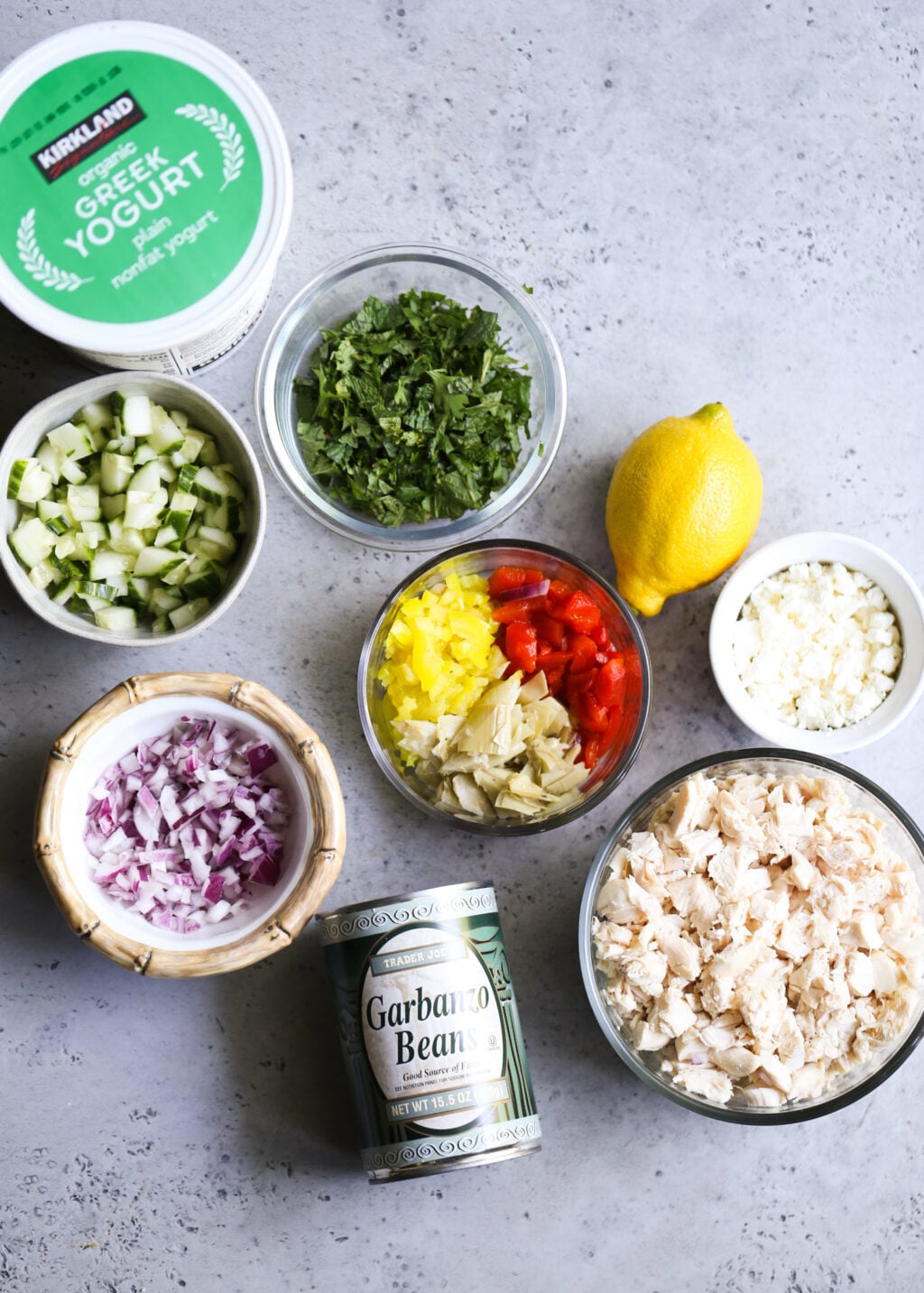 Mediterranean chicken salad ingredients: shredded chicken, chickpeas, cucumber, red onion, artichokes, peppers, feta, yogurt, lemon.
