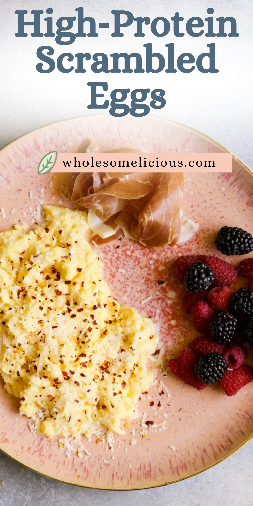 Pink plate of high-protein scrambled eggs with cottage cheese, red pepper flakes, prosciutto, and berries - breakfast recipe.