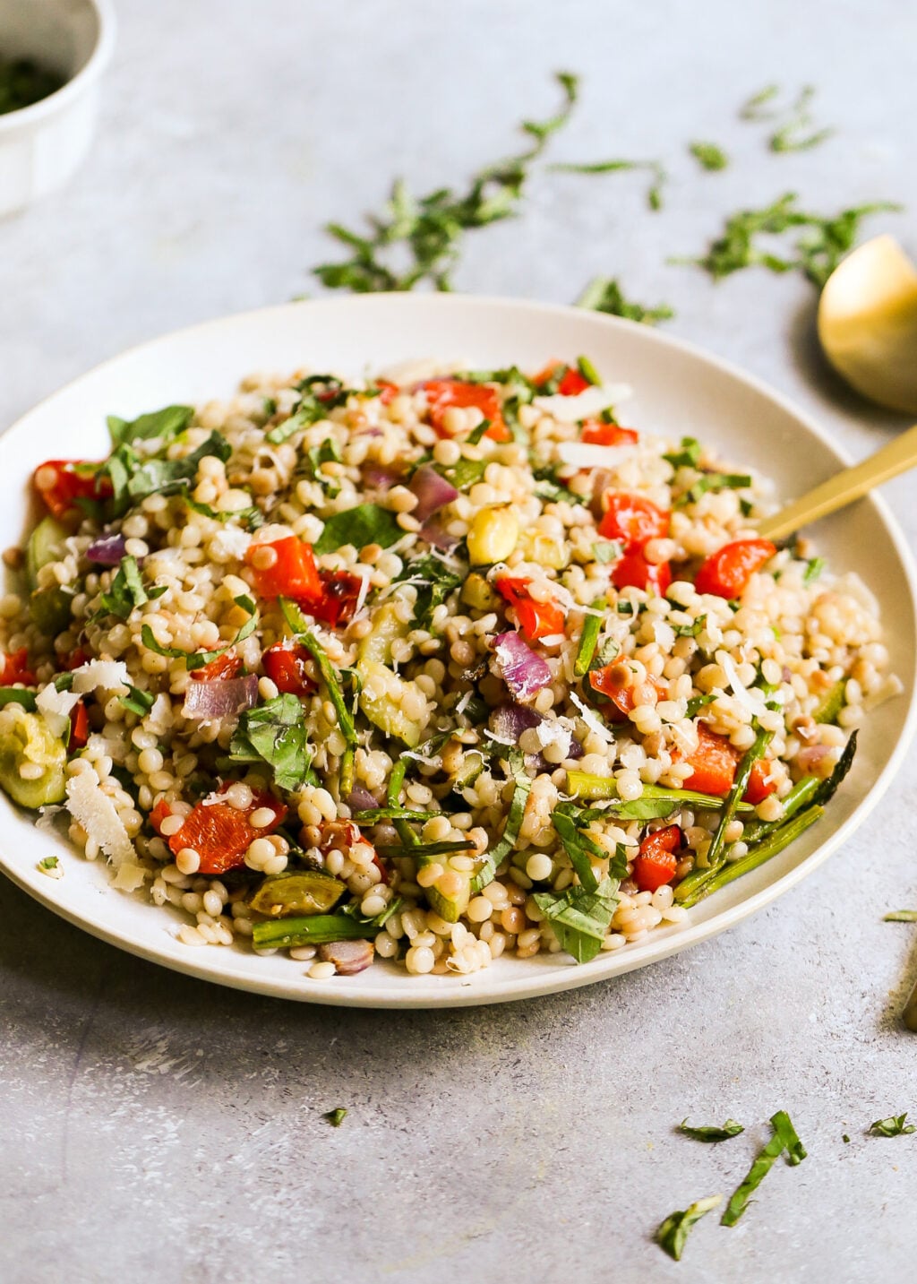 Israeli couscous salad with roasted vegetables, fresh herbs, and Parmesan served on a plate for a healthy side dish.
