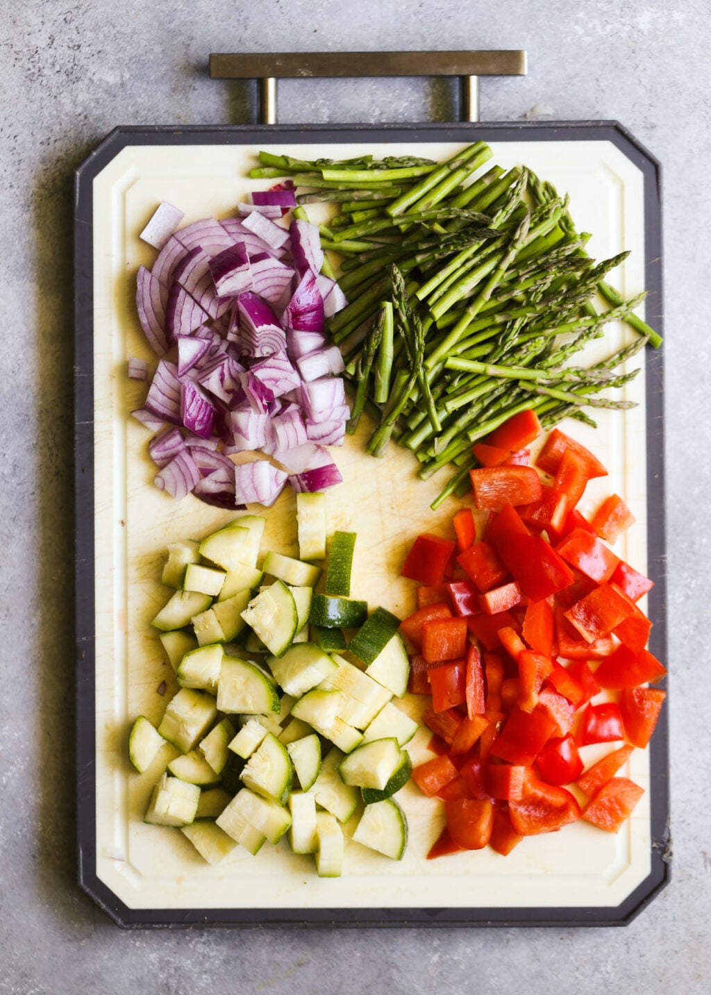 Chopped zucchini, bell pepper, asparagus, and red onion prepped on a cutting board for roasted vegetable couscous salad.