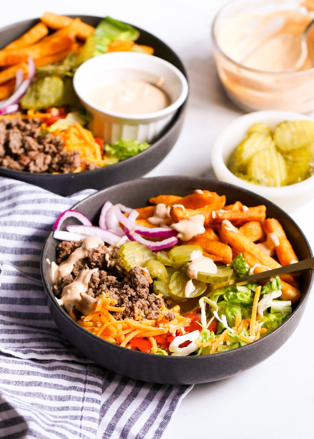 Deconstructed cheeseburger salad bowls with ground beef, cheese, pickles, onions, lettuce, and cottage cheese sauce.