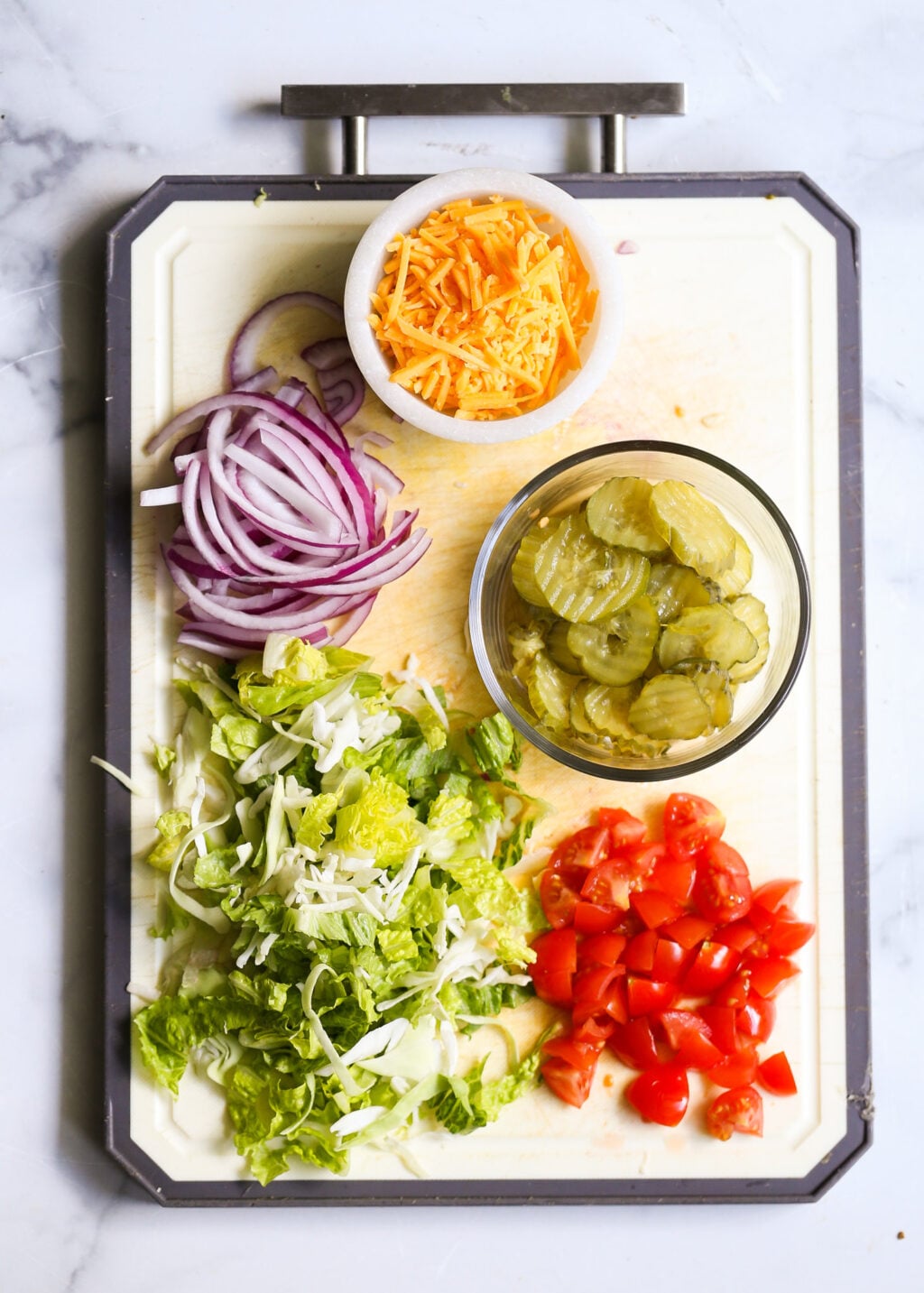 Fresh burger bowl toppings including lettuce, tomato, onion, cheddar cheese, and pickles.