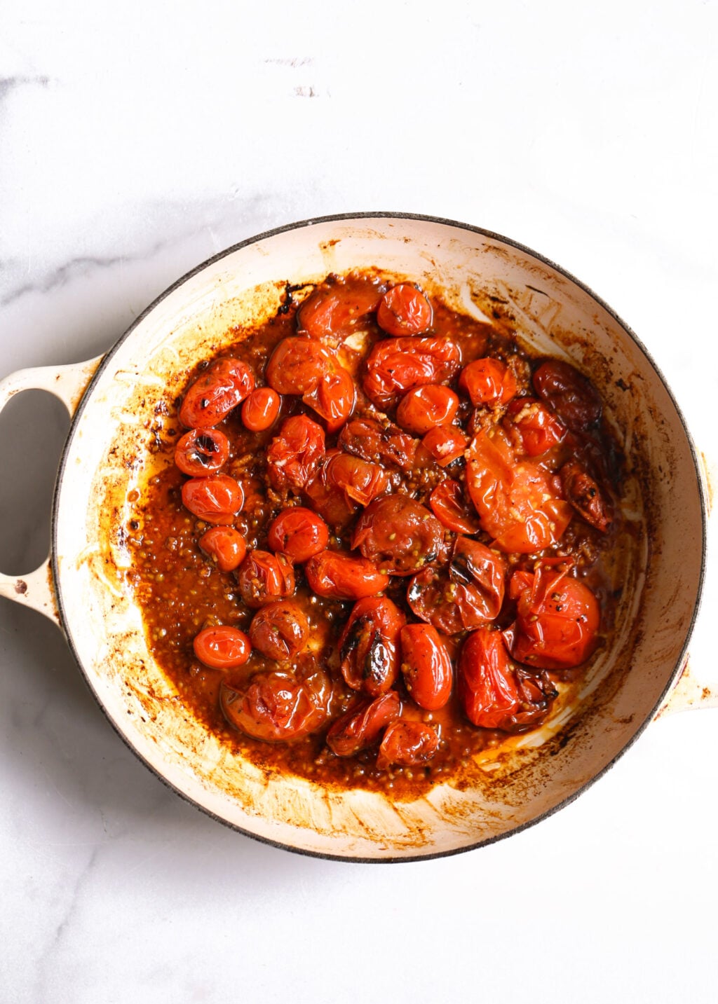 Burst cherry tomatoes roasted in a skillet to create a fresh tomato sauce for turkey and white bean skillet.